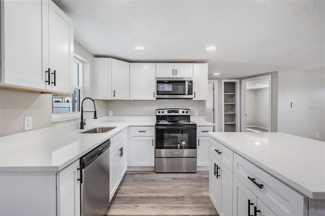 kitchen with sink, a textured ceiling, white cabinetry, stainless steel appliances, and light hardwood / wood-style floors