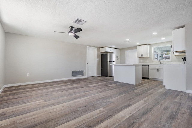 kitchen with white cabinets, stainless steel appliances, a center island, light hardwood / wood-style flooring, and sink