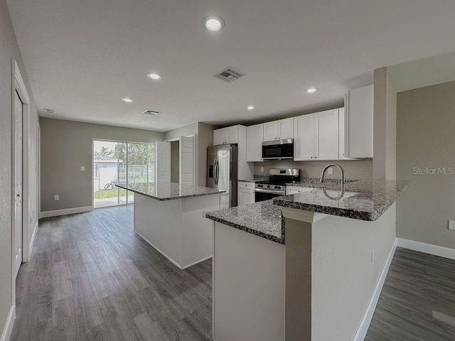 kitchen featuring kitchen peninsula, appliances with stainless steel finishes, dark stone counters, hardwood / wood-style flooring, and white cabinets