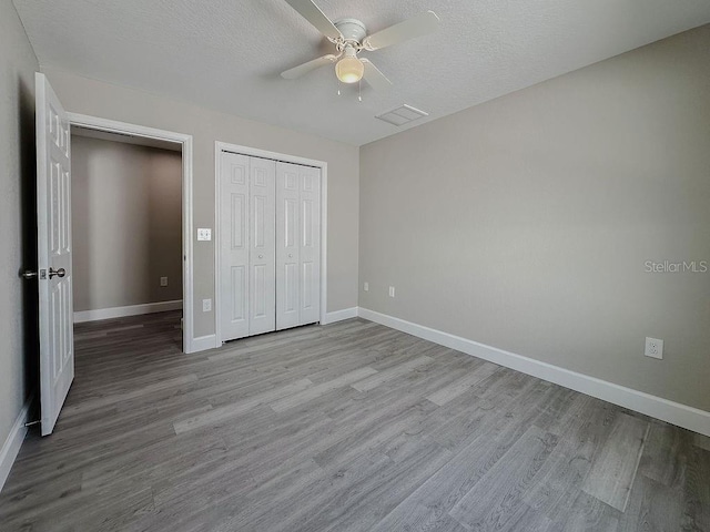 unfurnished bedroom with ceiling fan, a closet, a textured ceiling, and light wood-type flooring