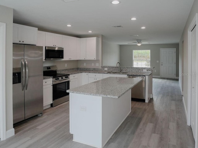 kitchen with light wood-type flooring, stainless steel appliances, sink, white cabinets, and a center island