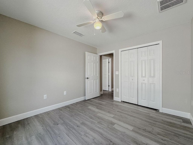 unfurnished bedroom with a textured ceiling, light wood-type flooring, a closet, and ceiling fan