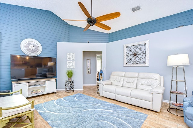 living room with wooden walls, high vaulted ceiling, light wood-type flooring, and ceiling fan