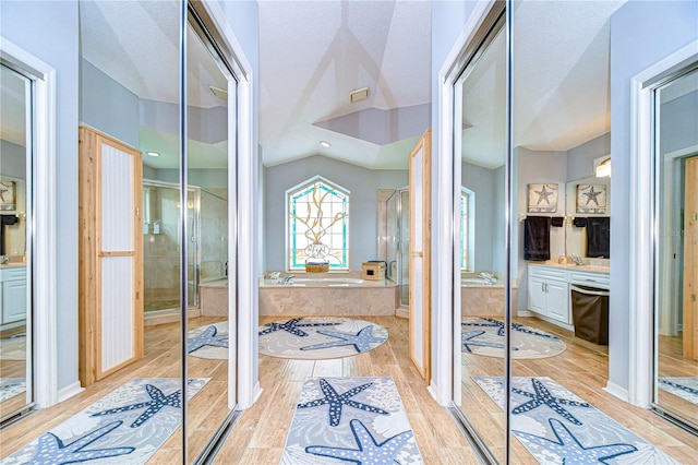 bathroom with vanity, independent shower and bath, lofted ceiling, and hardwood / wood-style floors