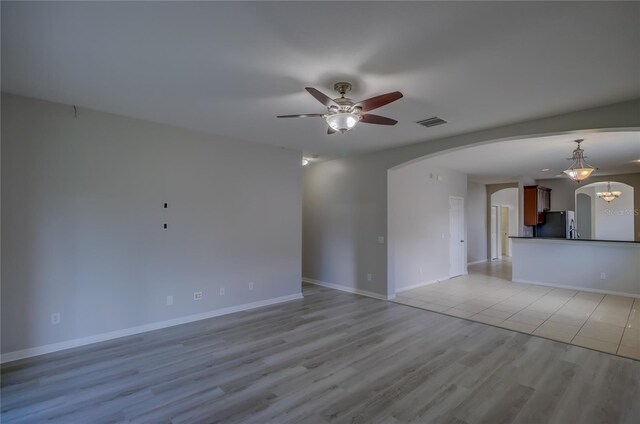 unfurnished living room with ceiling fan with notable chandelier and light hardwood / wood-style flooring