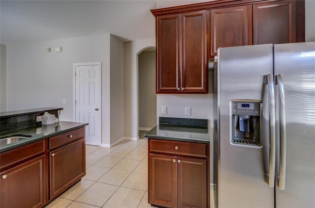 kitchen featuring dark stone counters, light tile patterned floors, stainless steel fridge with ice dispenser, and sink