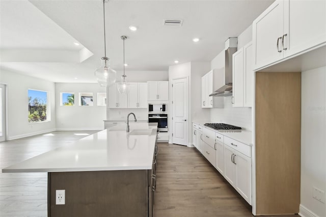 kitchen featuring pendant lighting, a center island with sink, white cabinets, wall chimney exhaust hood, and appliances with stainless steel finishes