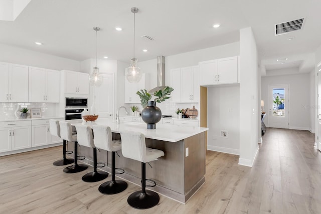 kitchen with white cabinetry, wall chimney exhaust hood, a kitchen island with sink, and built in microwave