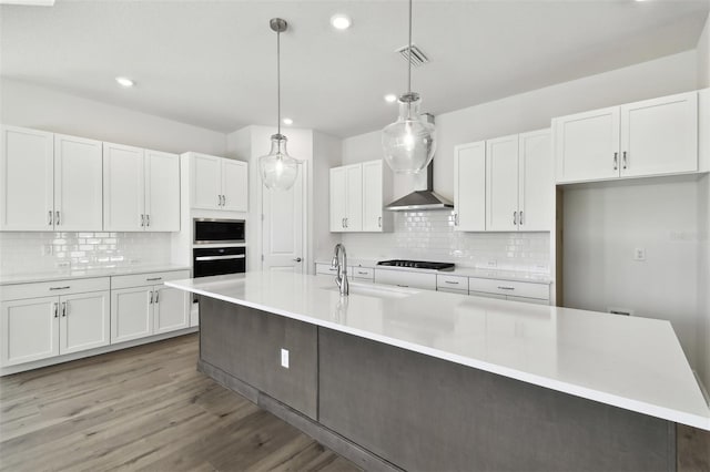 kitchen featuring stainless steel microwave, pendant lighting, wall oven, a kitchen island with sink, and white cabinets