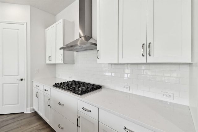 kitchen featuring wall chimney exhaust hood, stainless steel gas cooktop, white cabinetry, light stone counters, and backsplash