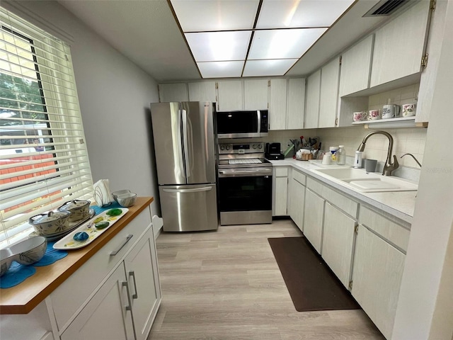 kitchen featuring appliances with stainless steel finishes, light wood-type flooring, sink, white cabinetry, and backsplash