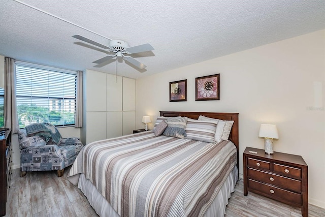 bedroom with light wood-type flooring, ceiling fan, and a textured ceiling