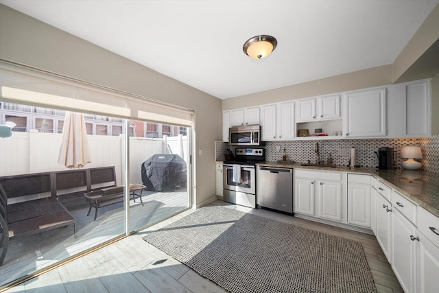 kitchen with sink, white cabinets, light hardwood / wood-style flooring, stainless steel appliances, and backsplash