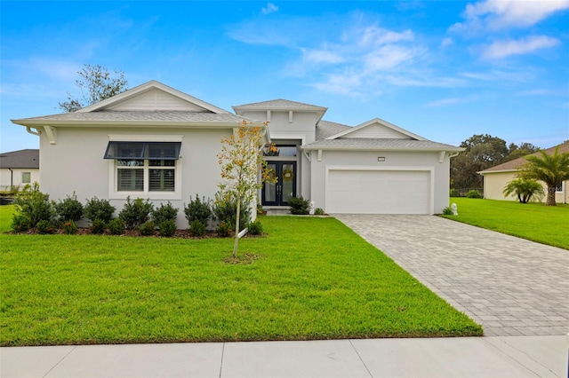 view of front of house with an attached garage, french doors, decorative driveway, stucco siding, and a front lawn