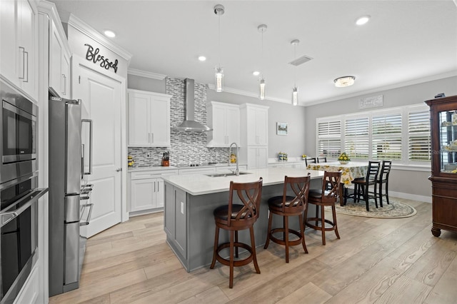 kitchen featuring appliances with stainless steel finishes, ornamental molding, light countertops, wall chimney range hood, and a sink