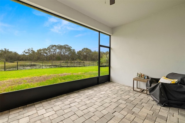 unfurnished sunroom featuring a ceiling fan and a rural view