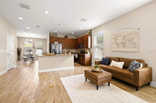 living room featuring a notable chandelier, light hardwood / wood-style floors, sink, and a wealth of natural light