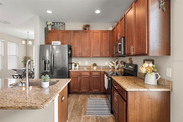kitchen featuring stainless steel appliances, a sink, light wood-style floors, brown cabinets, and light stone counters
