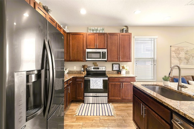 kitchen with appliances with stainless steel finishes, light hardwood / wood-style floors, light stone countertops, a textured ceiling, and sink