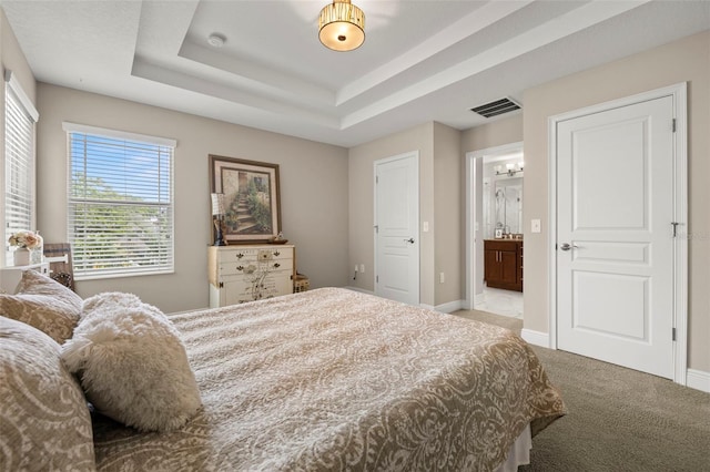 carpeted bedroom with baseboards, ensuite bathroom, visible vents, and a tray ceiling