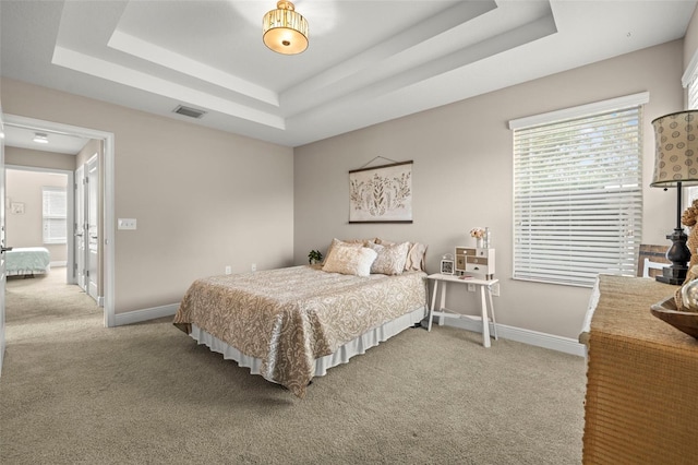 carpeted bedroom featuring a tray ceiling, visible vents, and baseboards