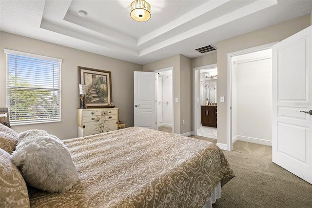 bedroom featuring visible vents, baseboards, light colored carpet, ensuite bath, and a raised ceiling