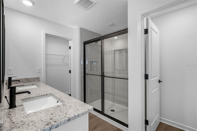 bathroom featuring wood-type flooring, a textured ceiling, walk in shower, and vanity