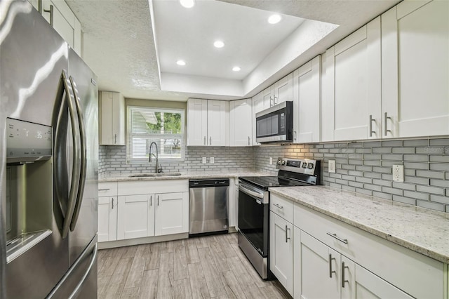 kitchen with a raised ceiling, appliances with stainless steel finishes, white cabinetry, light wood-type flooring, and sink