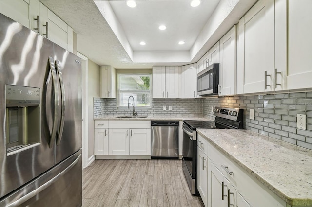 kitchen featuring sink, light stone countertops, white cabinetry, appliances with stainless steel finishes, and light hardwood / wood-style floors