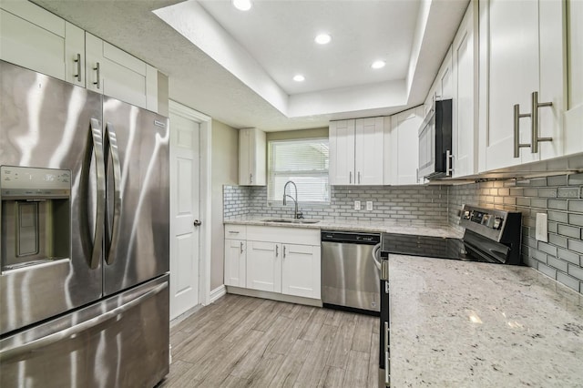 kitchen featuring white cabinets, light stone countertops, light hardwood / wood-style flooring, sink, and stainless steel appliances