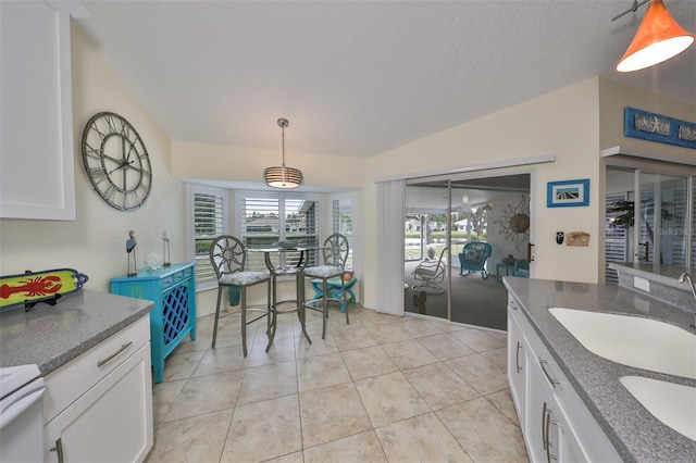 kitchen with lofted ceiling, hanging light fixtures, white range oven, light tile patterned flooring, and white cabinetry