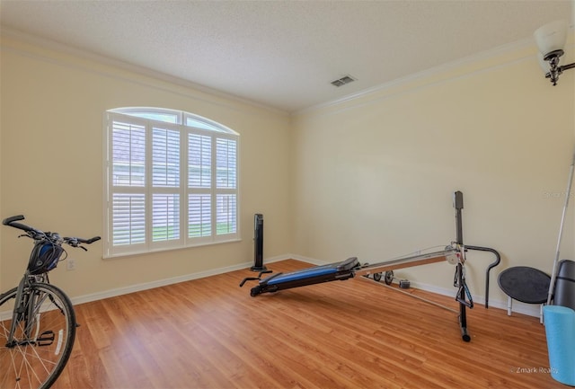 exercise room featuring wood-type flooring, a textured ceiling, and ornamental molding