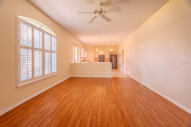 unfurnished living room with ceiling fan, a textured ceiling, and light wood-type flooring