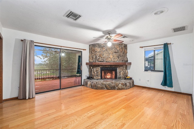 unfurnished living room featuring ceiling fan, light hardwood / wood-style floors, a stone fireplace, and a textured ceiling