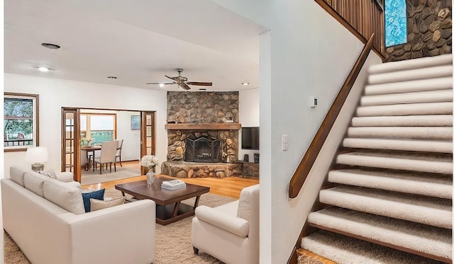 living room featuring light wood-type flooring, a stone fireplace, and ceiling fan