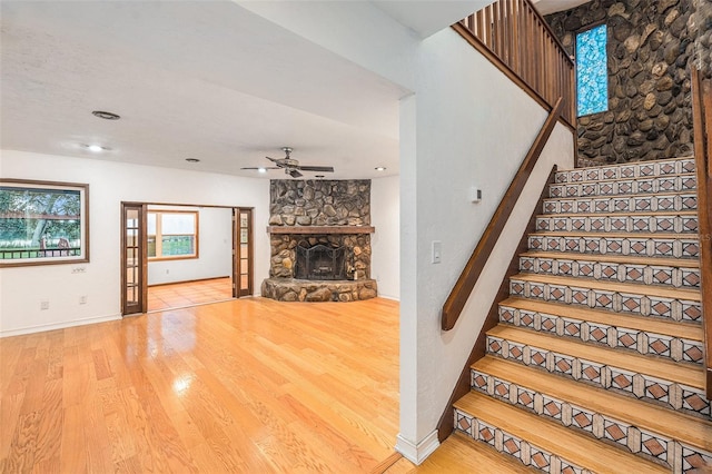 stairs featuring a fireplace, wood-type flooring, and ceiling fan