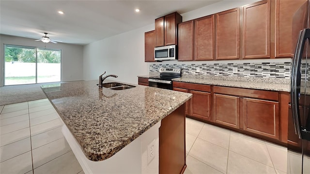 kitchen with appliances with stainless steel finishes, decorative backsplash, an island with sink, light stone countertops, and sink