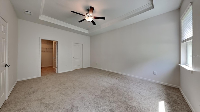 unfurnished bedroom featuring a closet, crown molding, a tray ceiling, ceiling fan, and a walk in closet