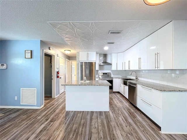 kitchen with wall chimney exhaust hood, white cabinetry, stainless steel appliances, a center island, and hardwood / wood-style floors