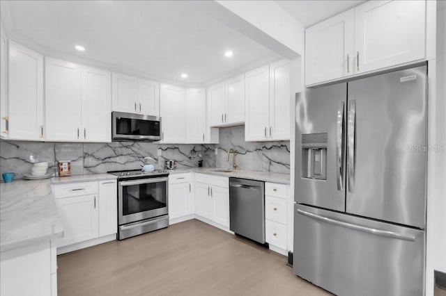 kitchen featuring light wood-type flooring, tasteful backsplash, white cabinets, stainless steel appliances, and light stone countertops