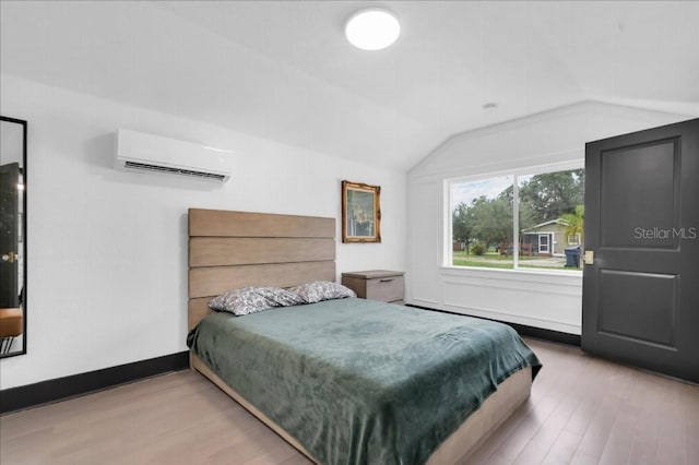 bedroom with light wood-type flooring, vaulted ceiling, and an AC wall unit