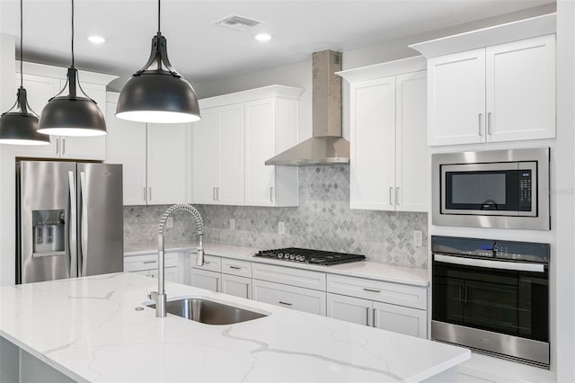 kitchen featuring appliances with stainless steel finishes, white cabinets, wall chimney exhaust hood, light stone countertops, and decorative light fixtures