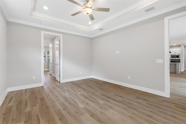 empty room with crown molding, light hardwood / wood-style floors, and a tray ceiling