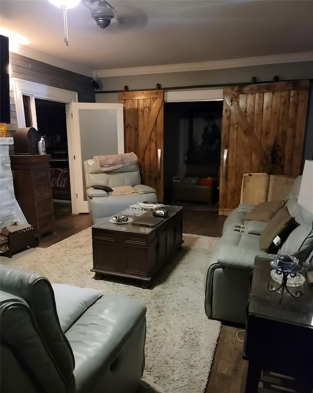 living room with a barn door, dark hardwood / wood-style flooring, crown molding, ceiling fan, and wooden walls