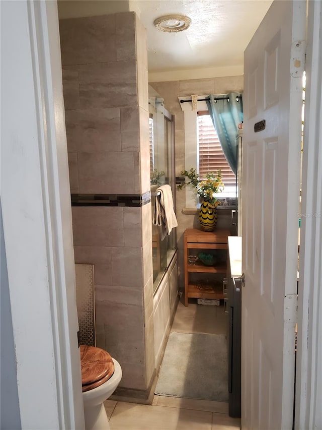 bathroom with bath / shower combo with glass door, tile patterned floors, and toilet