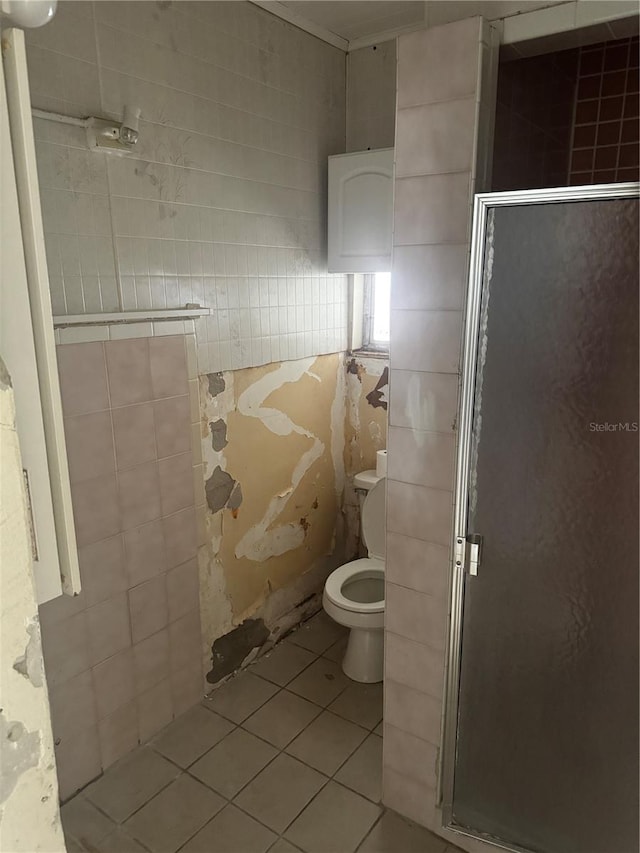 bathroom with tile patterned flooring, toilet, a shower with shower door, and tile walls