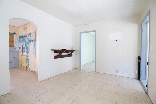 empty room featuring arched walkways and light tile patterned flooring