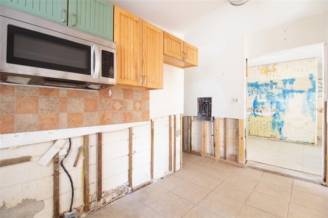 kitchen featuring light tile patterned floors, light brown cabinetry, stainless steel microwave, and backsplash