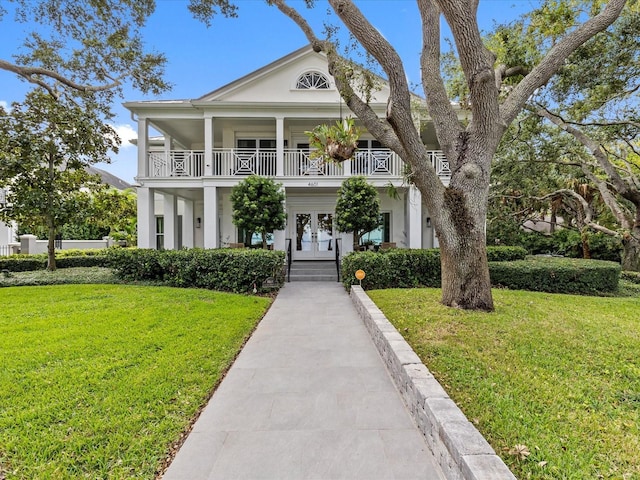 greek revival house with french doors, a front yard, a balcony, and covered porch