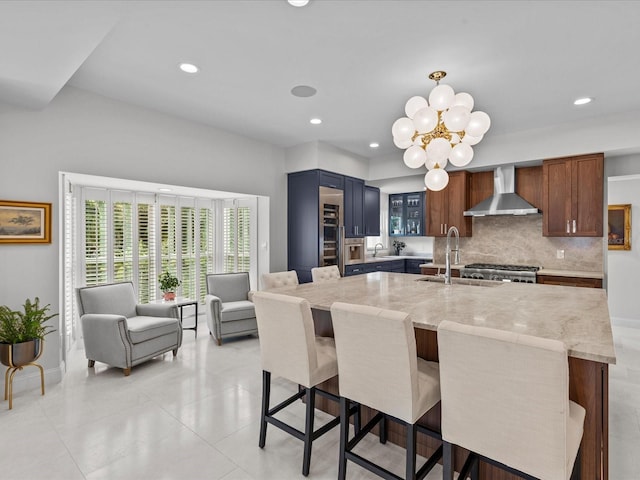 kitchen with wall chimney range hood, sink, light stone counters, backsplash, and a kitchen bar